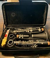 Clarinet disassembled inside a black carrying case with spare reeds and cleaning cloth visible