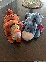 Orange Tigger and gray Eeyore plush stuffed animals on wood table