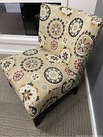 Front angle view of the upholstered accent chair highlighting the circular floral pattern on beige fabric and wooden legs.