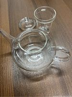 Top view of empty clear glass tea pot body, glass lid and a clear glass cup on wooden surface