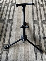 Guitar stand with tripod base and padded arms for instrument support lying on a patterned carpet.