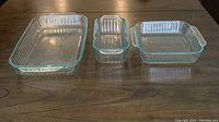Photo of three clear glass Pyrex baking dishes of different sizes with handles on wooden table
