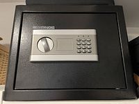 Black rectangular safe with electronic keypad and manual turn handle, Slypnos brand label visible on front.