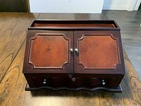 Closed wooden jewelry box with two front doors and silver knobs, placed on wooden table.