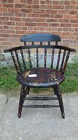Front view of antique captain's chair showing its distressed black painted wood and spindle backrest.