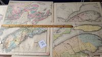 Photo showing three antique maps laid out side by side with a ruler for scale. The maps depict parts of the Dominion of Canada, including Quebec and Nova Scotia with detailed borders and colored regions.