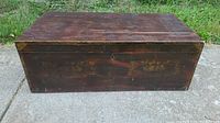 Frontal view of antique wooden storage box showing original floral stencil decoration and aged wood surface.