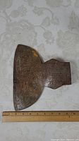 Top-view photo of rusty broad axe head placed next to measuring ruler showing length approximately 10 inches and width approximately 8 inches.
