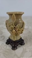 Front view showing floral carving on soapstone vase mounted on wooden stand.