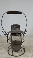 Front view of vintage metal hand lantern with wooden handle and perforated ventilated top.