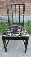 Front view of antique chair showing peeling black paint and three vertical spindles in the backrest.