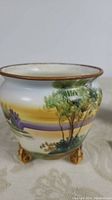 Front view of small tapered and footed Nippon vase with landscape painting and gold rim.