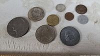 Top-down photo showing nine coins of various sizes and metals on a white patterned cloth.