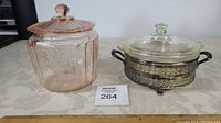 Photo showing pink Depression glass candy jar next to clear glass Pyrex casserole in silver-tone server on a table.