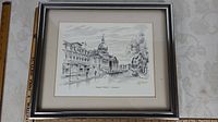 Framed black and white art print showing an urban street scene with architecture including a domed building, signed by Trudy Doyle.