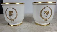 Two white ceramic wine chillers side by side showing gold rim and neoclassical motifs on front