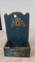 Front view of the hand decorated wooden wall mounted box, shows floral folk art painting and hole for hanging.