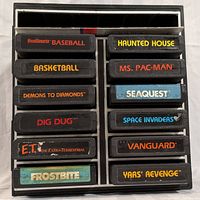 Top view of 12 Atari 2600 game cartridges arranged in two columns inside the black plastic storage organizer, showing colorful game labels.