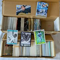 Top-down photo of three stacks of baseball cards in a cardboard box with several visible front and back cards showing Griffey Sr. and Jr. duo and Dream Team cards.