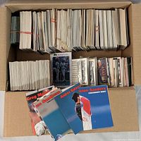 Box of assorted baseball cards in stacks showing variety of sizes and some individual cards with color photos and text