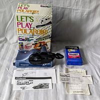 Full lot setup showing Polaroid Joycam 500 camera, unopened film box, and instruction manuals on a fabric background.
