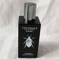 Front view of black rectangular Tokyo Milk Dark Arsenic Eau de Parfum bottle with insect illustration and silver cap.