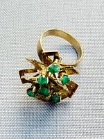 Front view of ring showing geometric cluster setting with multiple prong-set round emeralds