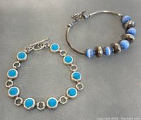 Two bracelets displayed on a gray surface showing overall design and color contrast: one with turquoise stones and one with blue glass beads.