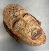Front angled view of the carved wooden tribal mask showing face details and weaving on sides.