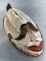 Front angled view of the antique wooden tribal mask showing white paint, black eyebrows, red lips, and natural wood edges with rope binding.