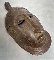 Angled top front view of the dark wooden mask showing facial features and patina.