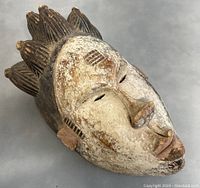 Close front view of the antique wooden tribal mask showing face details and textured top crest.