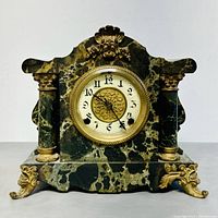 Front view of antique New Haven marble mantle clock showing ornate green marble body with gold accents and columns on each side, clock face with black numbers and floral gold center.
