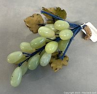 Front view of the green jade grape cluster showing the polished oval jade stones and carved agate leaves on blue stems.