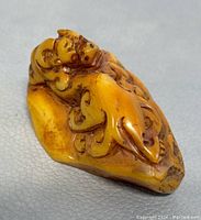 Side angle view showing detailed carving on the dragon figure in yellow-orange stone with dark brown accents.