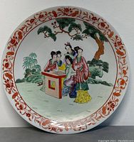 Front view of large 16 inch round Chinese porcelain platter with famille rose decoration of women playing board game outdoors and red floral border.