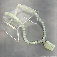 Full view of the necklace displayed on a clear stand showing round jade beads and elephant pendant.