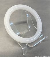 Photo of a white jade bangle displayed on a clear plastic stand showing its rounded, polished surface and shape.