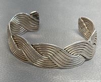 Close-up angled photo of the silver cuff bracelet showing the braided wave design, texture and patina.
