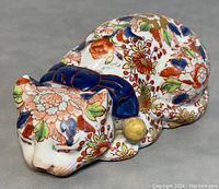Angle showing the front and side of the cat figurine with detailed multi-color floral decoration and blue collar with yellow bell.