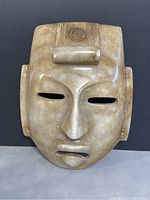 Front view of the vintage Mexican Aztec stone carved mask on a dark background, showing facial features and rectangular eye openings.