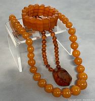 Full view of bracelet and two necklaces shown on a stand for scale