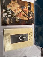 Photo of two hardcover books laying flat on a white sheet. The first book titled 'Enchanted Lives Enchanted Objects' shows a historical image of a woman in embroidered clothing with antiques. The second book titled 'Women's Culture' has a cream-colored dust jacket with a black-and-white image of a woman.