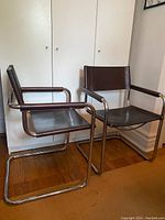 Two cantilever chairs with tubular metal frames and dark leather seats against white wardrobe background.