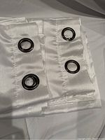 Two white curtain panels folded showing metal grommets for hanging on curtain rods.