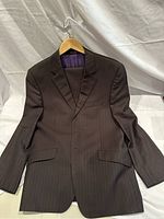 Front view of chocolate brown Paul Smith men's suit jacket with subtle light tan pinstripes hung on wooden hanger against white backdrop.