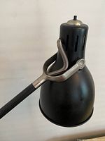 Close-up of black lamp shade with ventilation slots and silver-tone adjustable joint.