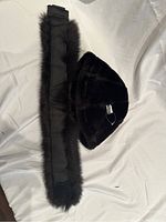 Black fox fur head band and black Roots acrylic hat laid flat on white surface.