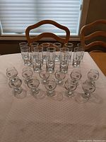 Photo showing 11 brandy glasses and 11 hi ball glasses arranged on a table with chairs behind.