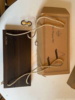 Wood hanging shelf laid flat showing attached ropes and mounting hardware, with its cardboard box labeled 'Wood Hanging Shelf'.